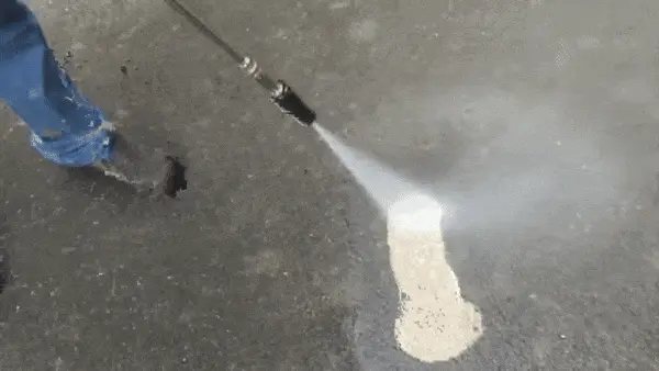 A high pressure jet stripping dirt from a concrete driveway in a clean stripe
